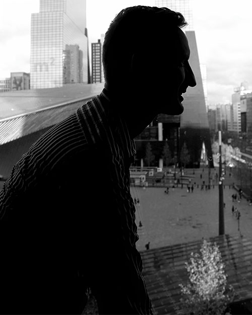 Silhouette of Jeremy Raes sitting in front of a window with a view over the square in front of Rotterdam Central Station
